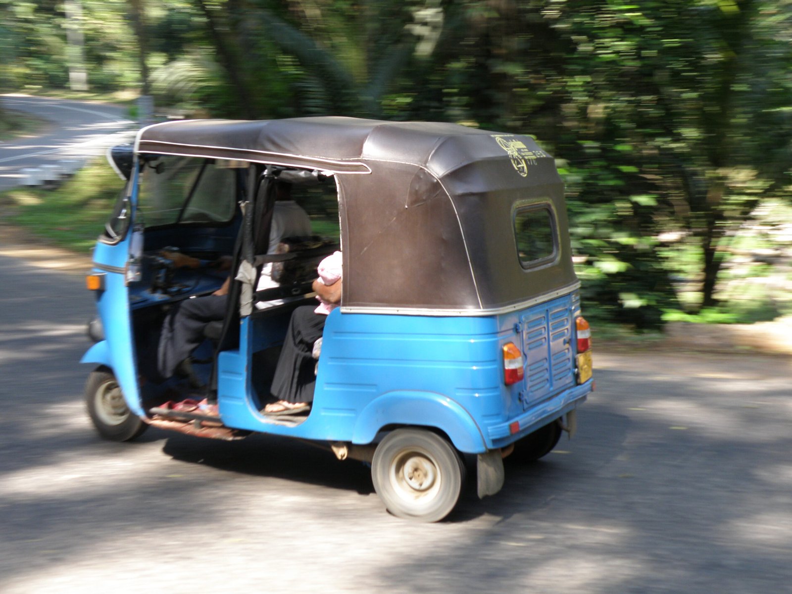 Blue tuk-tuk travelling along a leafy road in Akuressa, Sri Lanka; illustrative transport photograph